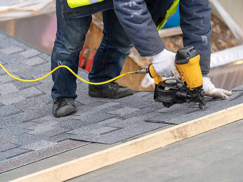 Close up of a worker installing new gray shingles on a residential roof