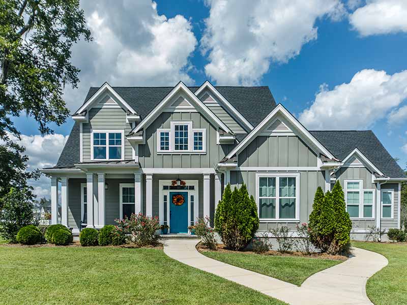 Front view of a mid-class, two-story light green home with a teal front door and dark gray asphalt shingles on its roof