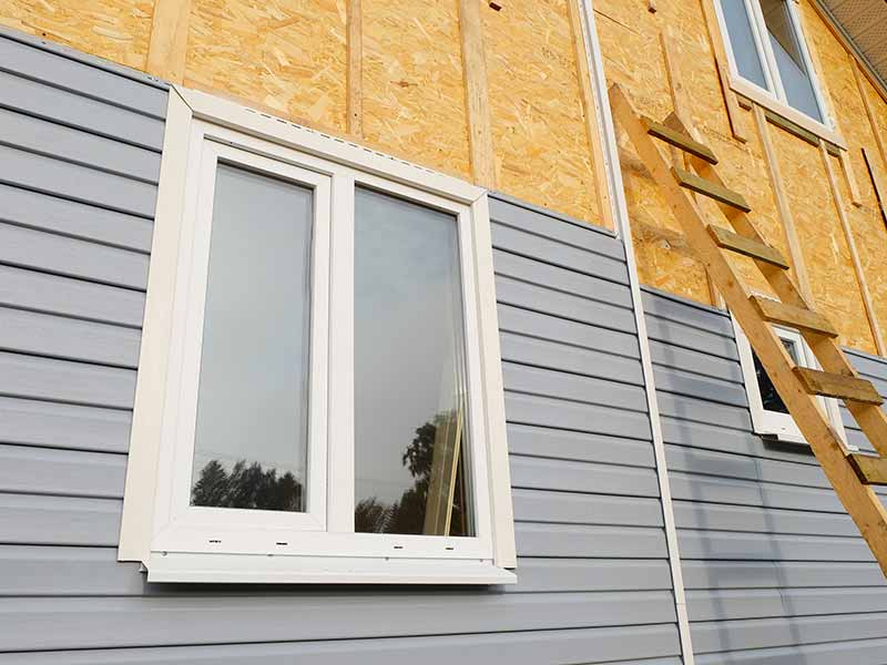 Side of a home in the process of getting new gray siding installed